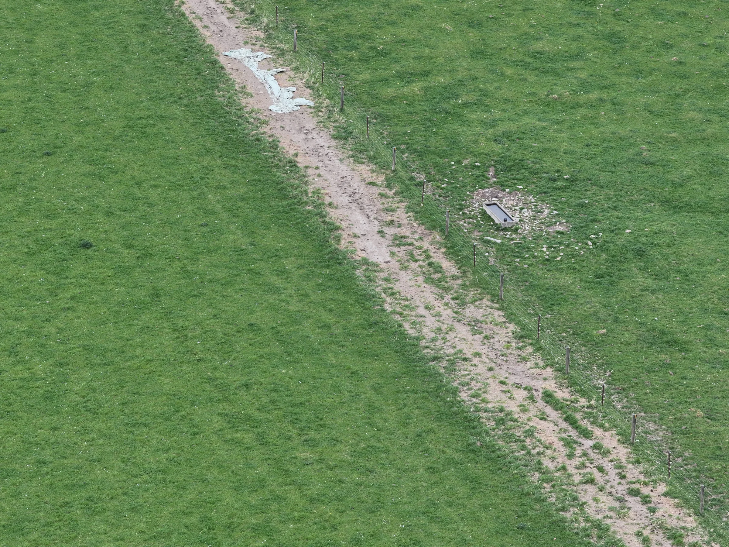 Aerial view of a worn paddock laneway beside a fence and water trough
