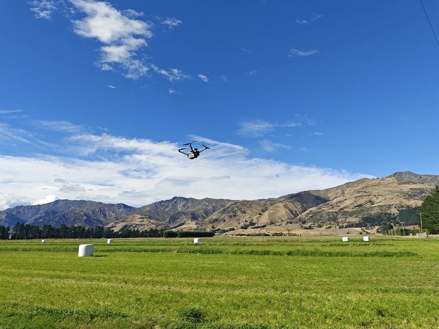 A drone flying above a green Hāwea farm with mountains beyond